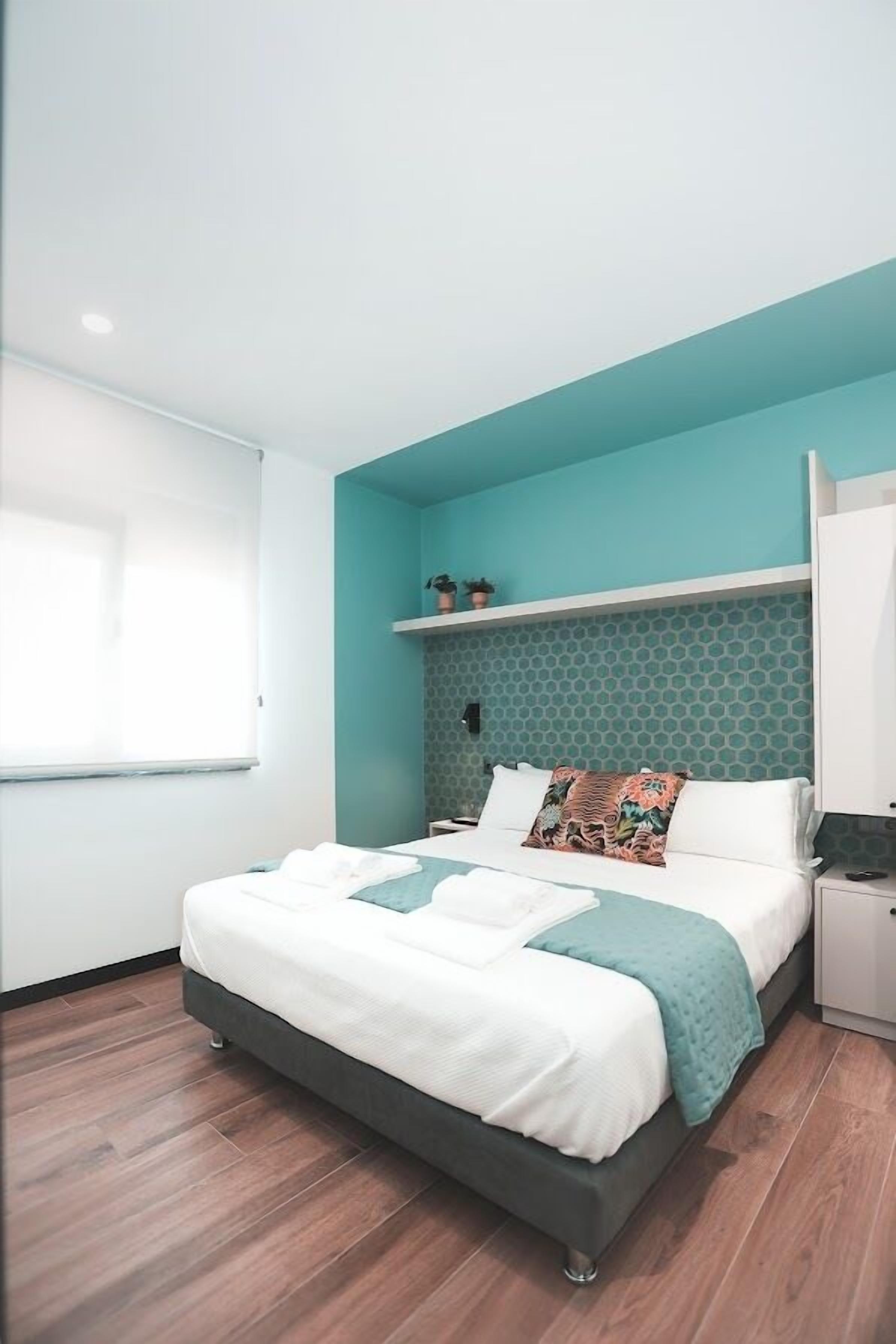 A modern bedroom with a bed, a nightstand, a window, and a wall with a geometric pattern.