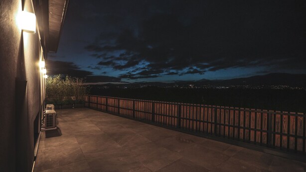 Vista noturna de uma varanda com guarda-corpo, uma pequena mesa e um vaso de planta.