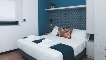 A modern hotel room with a bed, a nightstand, a wardrobe, and a window with blinds.