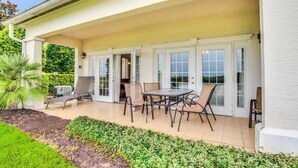 Une terrasse couverte avec une table et des chaises, un palmier et un jardin bien entretenu.