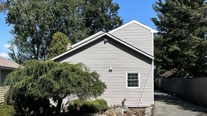 A single-story house with a sloped roof, a small window, and a well-maintained front yard with rocks and a tree.