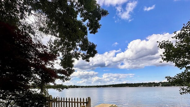 A wooden dock extending into a calm lake, surrounded by trees and a clear sky.