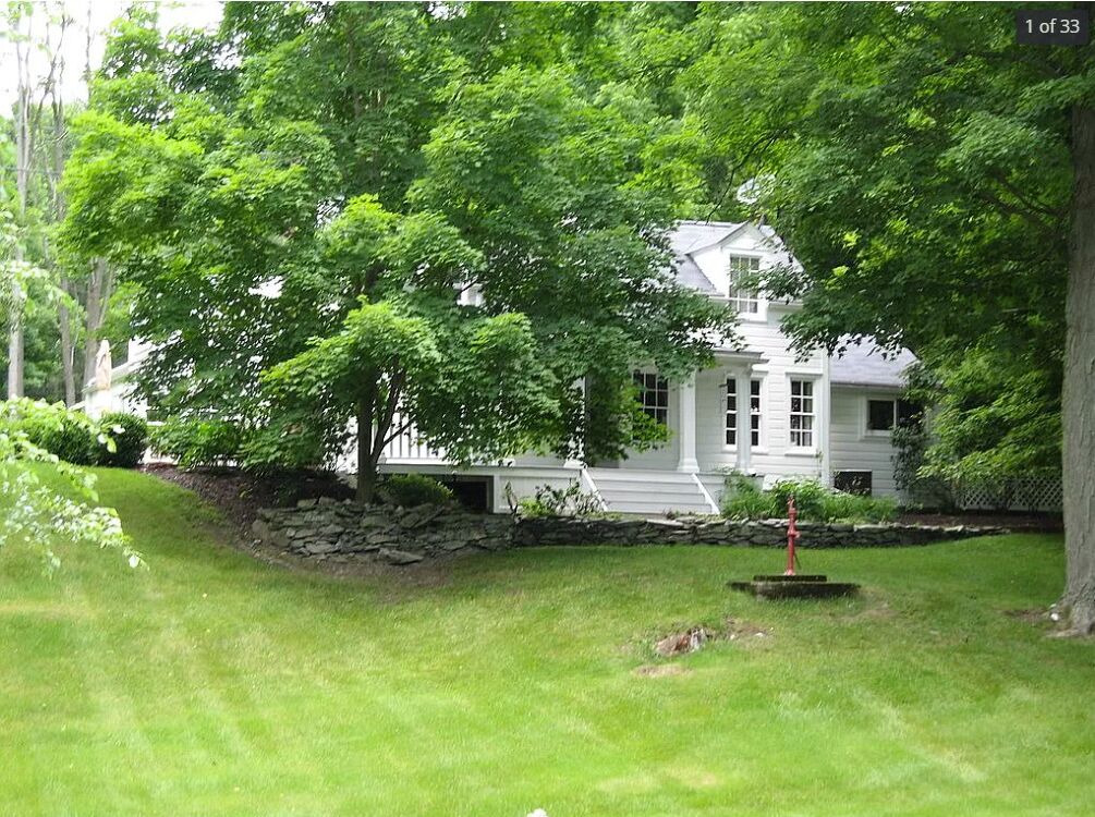 A white house with a stone wall and a well-maintained lawn.
