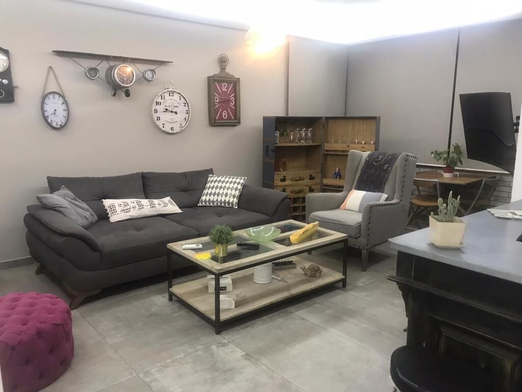 Un salon comprenant un canapé, une table basse et un téléviseur. On y trouve également des horloges au mur et un meuble contenant divers objets.