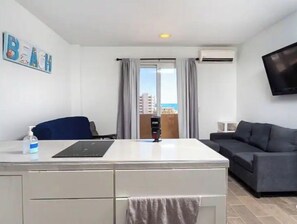 Hotellihuone, jossa on työpöytä, tuoli, sohva, televisio, ikkuna verhoilla ja näkymä rakennuksiin.