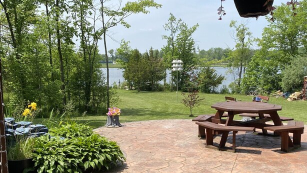 Un espace extérieur aménagé en terrasse, doté d’un sol en pierre, entouré de verdure et offrant une vue sur un lac.