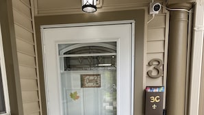 Une porte d’entrée blanche avec un panneau de verre, une boîte aux lettres et un panneau portant le chiffre « 3 » fixé au mur.