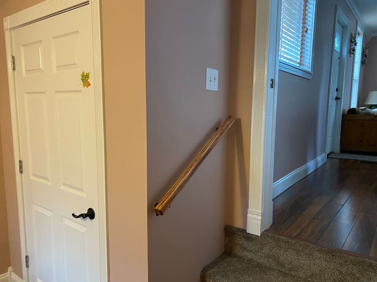 Un couloir avec une porte blanche, une main courante en bois et un sol recouvert de moquette.