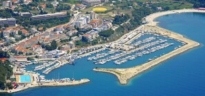 Vista aérea de una marina costera con numerosas embarcaciones amarradas, rodeada de edificios residenciales y una playa de arena.