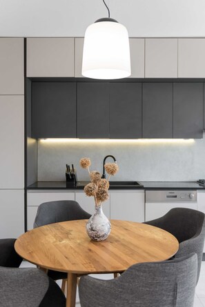 A modern kitchen with a round wooden table, grey upholstered chairs, and a vase with dried flowers. - Modern apartment Marija with the balcony and the sea view (Split)