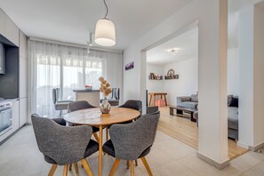 Un salon moderne avec une table ronde en bois, des fauteuils à revêtement gris, un canapé et un coin repas agrémenté d’un vase blanc.