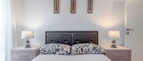 A bedroom with a bed, two bedside tables with lamps, a door, and three framed pictures on the wall.
