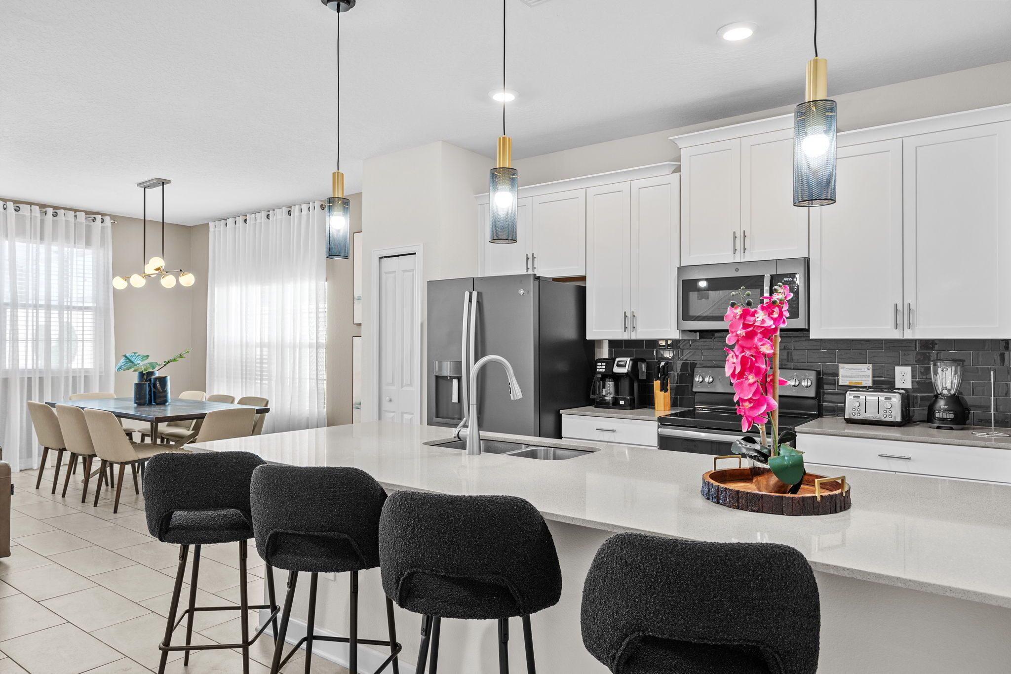 A modern kitchen with white cabinets, a central island with bar stools, a refrigerator, and a coffee machine.