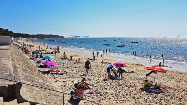 Ein Strand mit badenden Personen, Sonnenschirmen und Booten im Wasser.