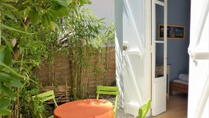 Eine kleine Terrasse im Freien mit einem runden Tisch und zwei Stühlen, umgeben von Bambuspflanzen und einer Backsteinmauer.