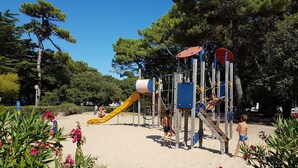 Ein Spielplatz mit verschiedenen Klettergerüsten und Rutschen, umgeben von Bäumen und Blumen.