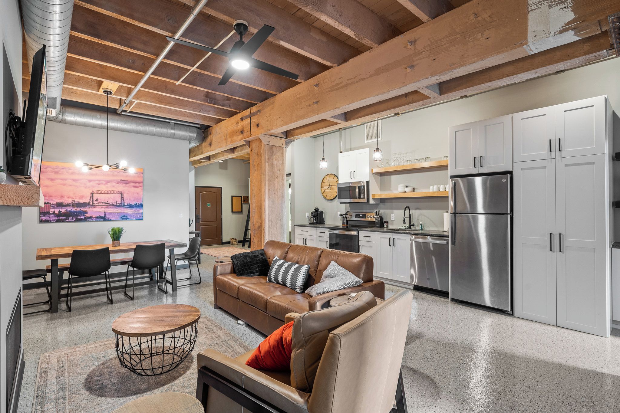 A modern kitchen with stainless steel appliances, a dining area with a wooden table and chairs, and a living room with a leather sofa and a coffee table.