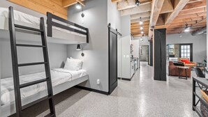 A bunk bed room with a ladder, a desk, and a chair. There is a door leading to another room. - Aurora Black | The Brix | Pool in Canal Park! (Duluth)