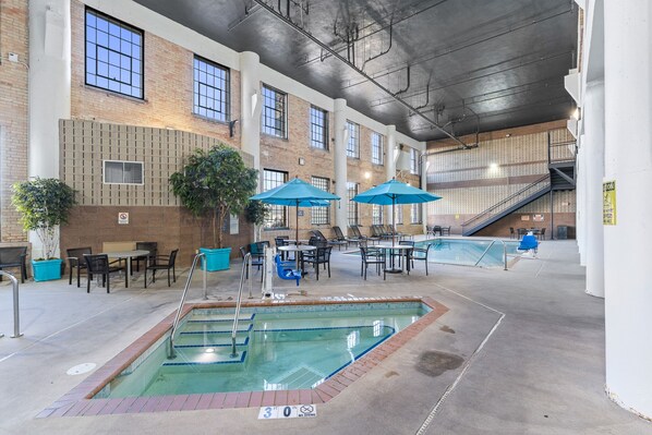 An indoor swimming pool area with multiple pools, lounge chairs, and umbrellas.