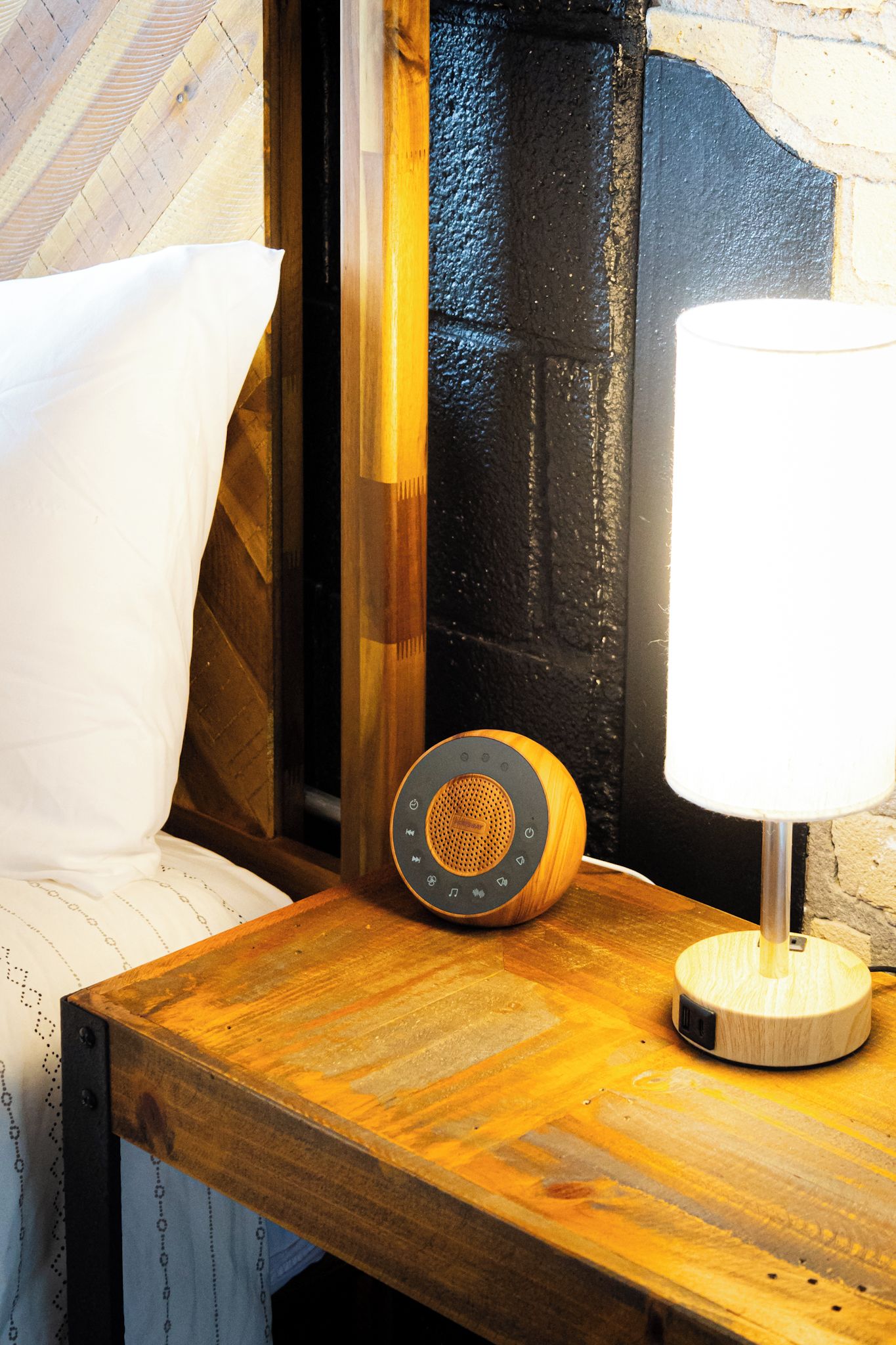 A wooden bedside table with a lamp and a speaker.