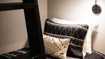 Ein Stockbett mit schwarzer Leiter, einer gemusterten schwarz-weißen Decke und einer einzelnen schwarzen Wandlampe.