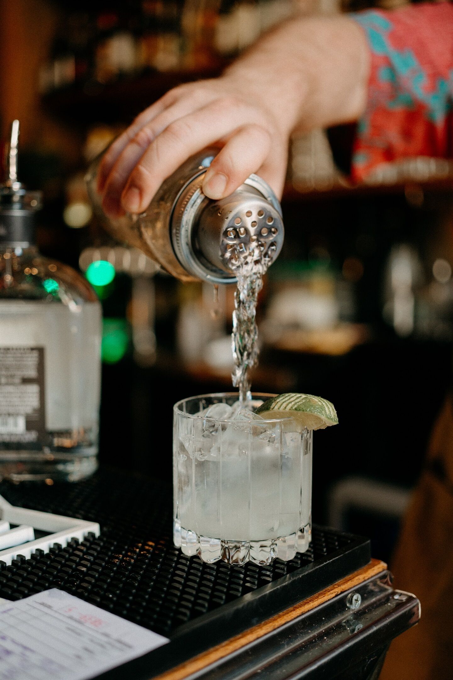 A hand pouring a clear liquid into a glass with ice cubes and a lime wedge.