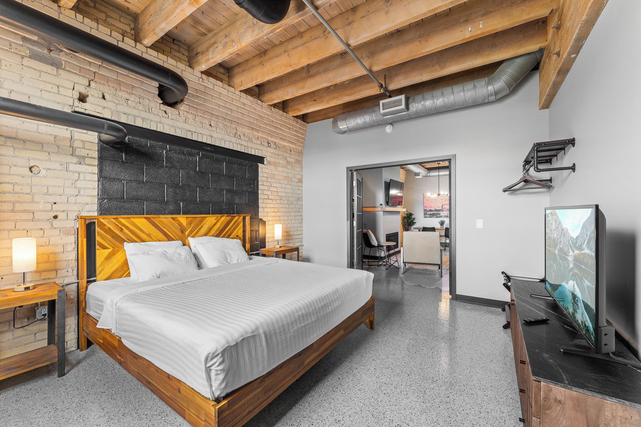 Une chambre d’hôtel moderne avec un lit en bois, une télévision et un mur en briques.
