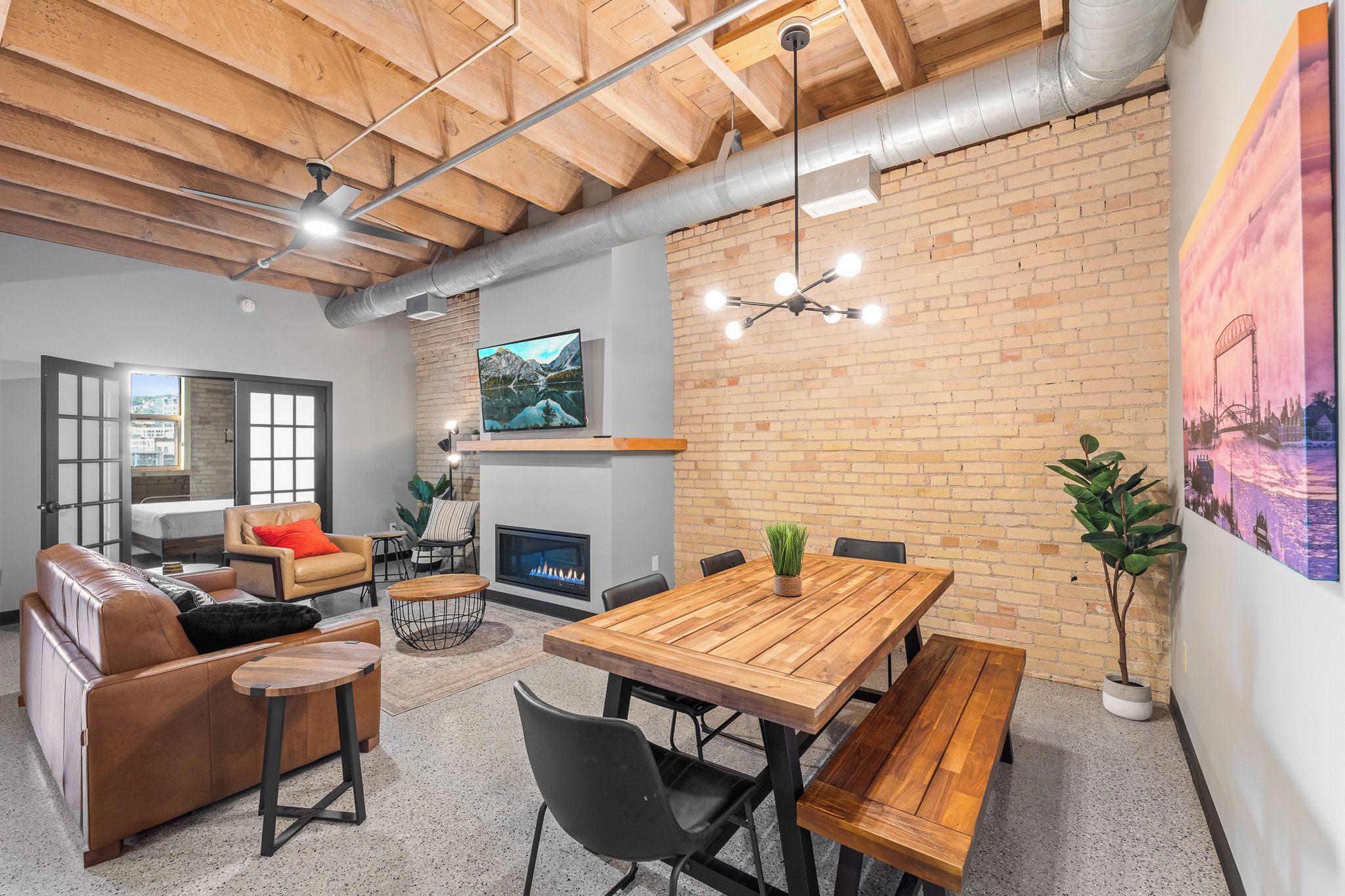 A modern living space with a wooden ceiling, a fireplace, a dining table with benches, and a large window.