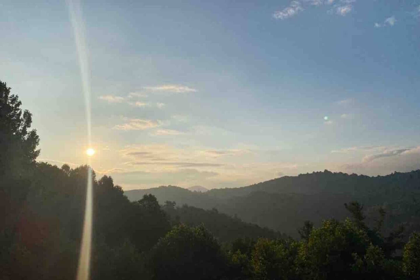 A landscape with a sun setting or rising behind a range of hills.