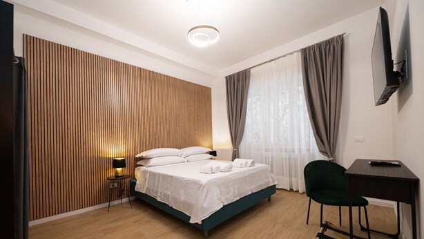 Quarto de hotel moderno com parede de ripas de madeira, cama com roupa branca, escrivaninha com cadeira e TV fixada na parede.