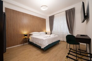 A modern hotel room with a wooden slat wall, a bed with white linens, a desk with a chair, and a TV mounted on the wall. - Domus Vatican Holiday (Rome)