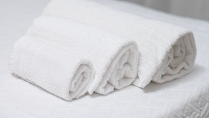 Toalha branca dobrada cuidadosamente sobre um lençol texturizado branco.