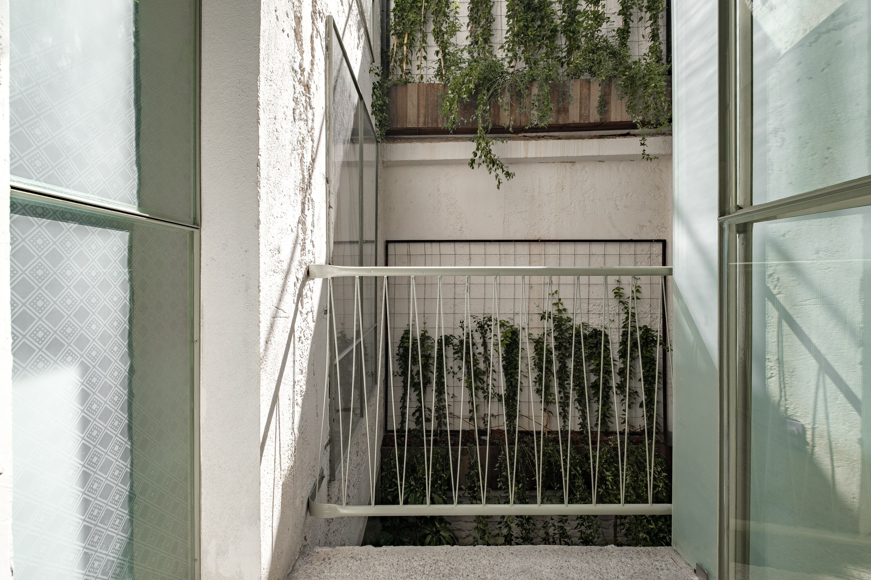 A narrow outdoor staircase with a metal railing, surrounded by walls with a textured finish and a window with a geometric pattern.