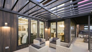 Un área de estar exterior moderna con mobiliario de mimbre y puertas de cristal que dan a un espacio interior.