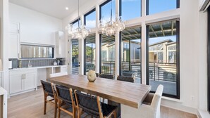 Una cocina moderna con una mesa de comedor de madera, armarios blancos y ventanas amplias que ofrecen vistas a un balcón.