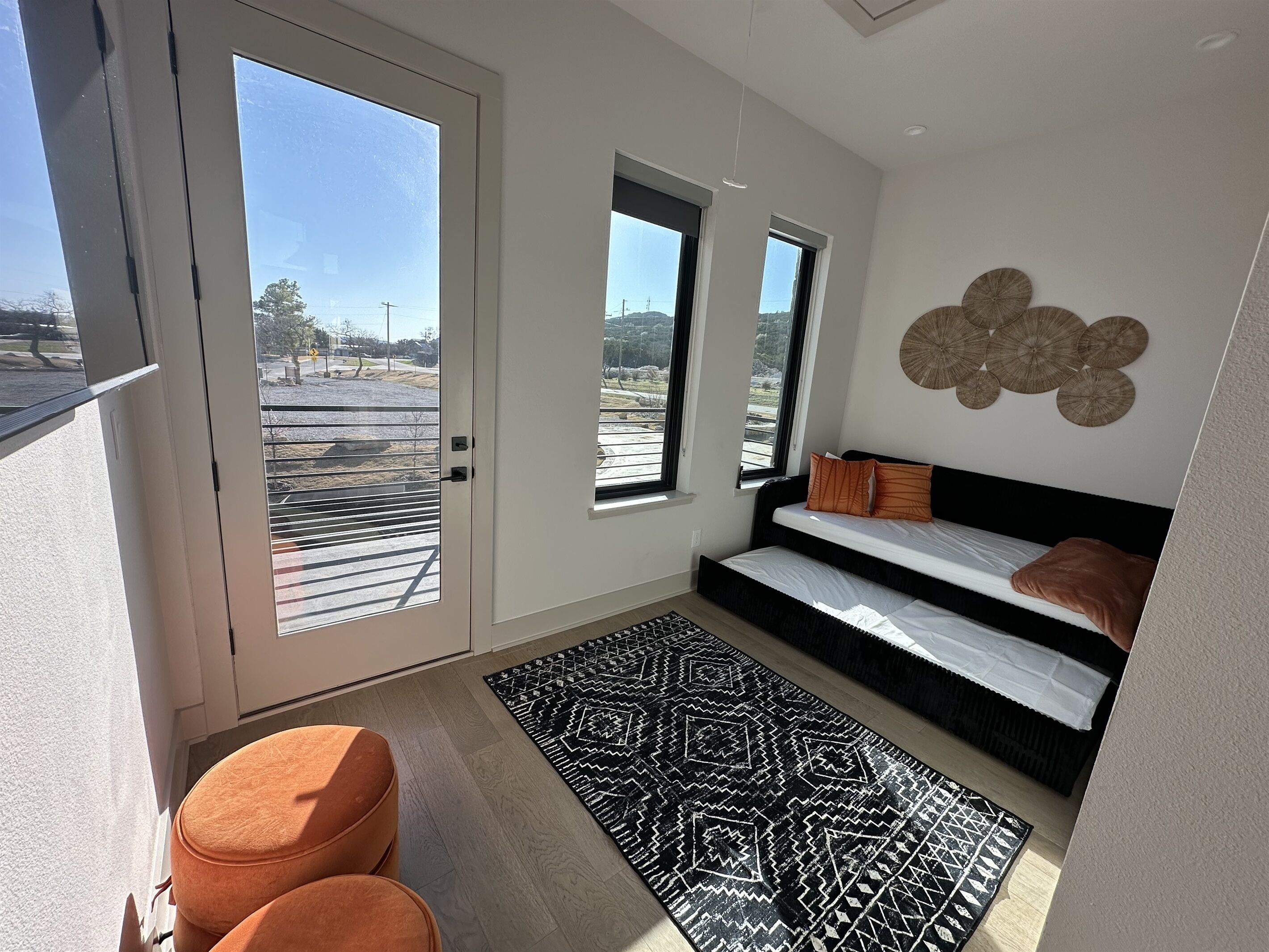 A modern bedroom with a large window, a black and white patterned rug, and a black bed with orange pillows.