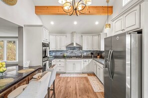Una cocina moderna con armarios blancos, un refrigerador de acero inoxidable y techo de madera.