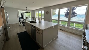 A modern kitchen with a large island, a dining area, and a view of a lake. - Waterfront Lakehouse - Completely Remodeled - Watersports + Hot Tub (Elk Rapids)