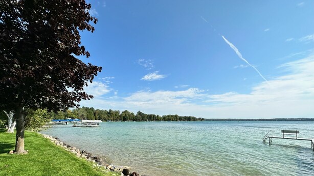 A lakeside park with a grassy area, a rocky shoreline, a dock, and a bench. - Waterfront Lakehouse - Completely Remodeled - Watersports + Hot Tub (Elk Rapids)