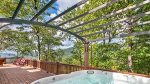 A hot tub on a wooden deck with a pergola overhead, surrounded by trees and a view of a mountainous landscape. - Black Bear Cabin w Majestic Views (Fairview)
