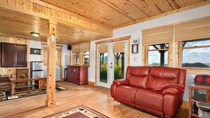 A cozy room with a wooden ceiling, a red leather sofa, a wooden cabinet, and a refrigerator. - Black Bear Cabin w Majestic Views (Fairview)