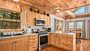 A spacious kitchen with wooden cabinets, stainless steel appliances, and large windows offering views of the outdoors. - Black Bear Cabin w Majestic Views (Fairview)