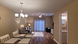 A dining area with a wooden table and chairs, a chandelier, and a sofa in the background.