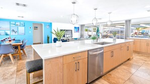 Una cocina moderna con una isla grande, electrodomésticos de acero inoxidable y un comedor con sillas azules y una mesa preparada para una comida.