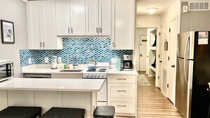 Uma cozinha moderna com armários brancos, um painel de backsplash azul estampado, fogão a gás, cafeteira e geladeira.