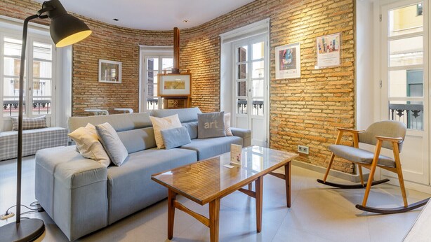 Una sala de estar con pared de ladrillo, un sofá, una mesa de centro, una lámpara de pie y un sillón mecedora.