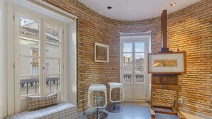 Una habitación con pared de ladrillo, puerta blanca, un banco, dos taburetes altos y un caballete de madera con una pintura.