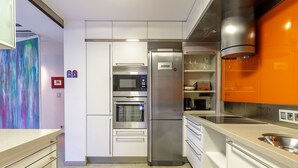 Una cocina moderna con electrodomésticos de acero inoxidable, armarios blancos y un cuadro abstracto y colorido en la pared.