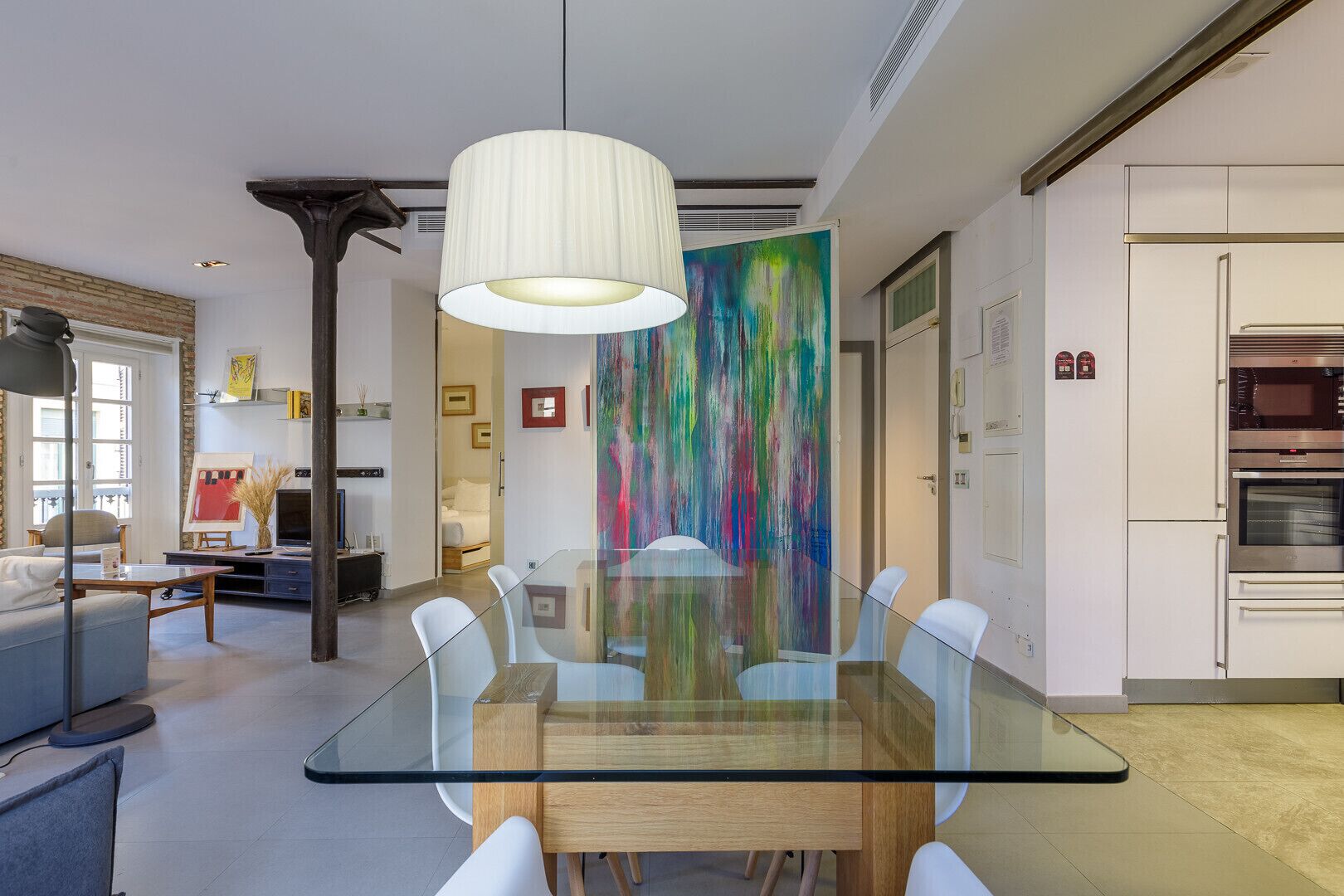 Zona pranzo moderna con tavolo in vetro, sedie bianche e un quadro astratto colorato appeso al muro.