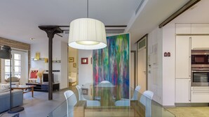 Un comedor moderno con una mesa de vidrio, sillas blancas y un cuadro abstracto colorido en la pared.